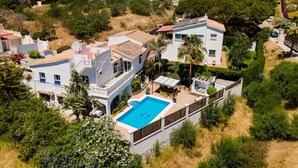 Zona residencial con una casa grande que tiene piscina, rodeada de vegetación y otras viviendas.
