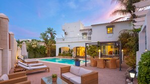 Un área junto a la piscina con sillones de descanso, un comedor y una pérgola.