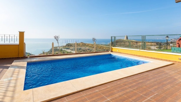 A rectangular swimming pool with clear blue water, surrounded by a wooden deck and a yellow wall. - Villa Margarita Villa Margarita Solset (Velez-Malaga)