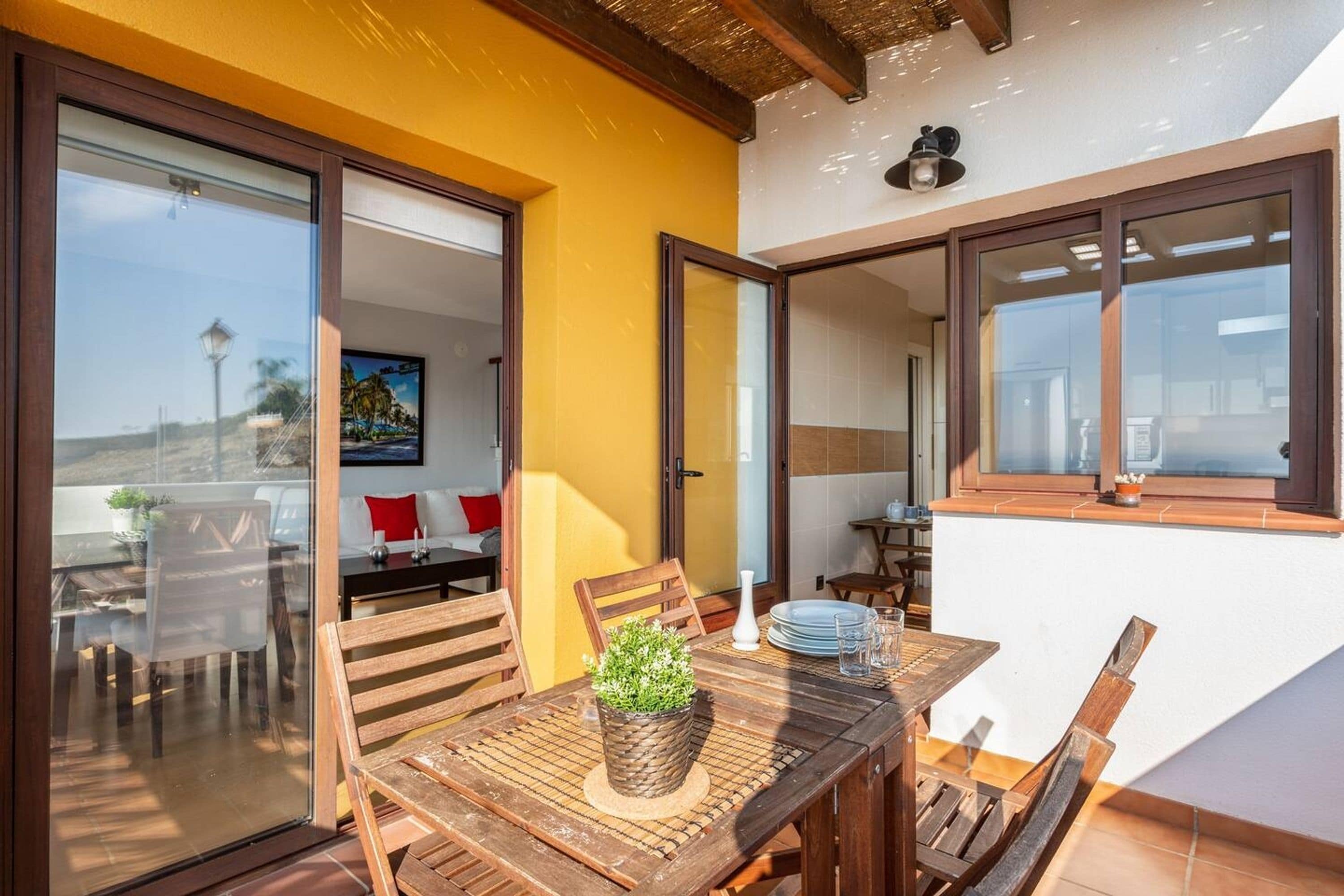 Un comedor con una mesa y sillas de madera, una planta en maceta y vistas al exterior.