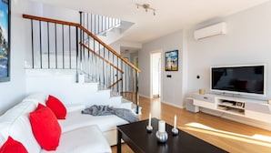 A modern living room with a staircase, white sofa, red cushions, a black coffee table, and a flat-screen TV. - Villa Margarita Villa Margarita Solset (Velez-Malaga)