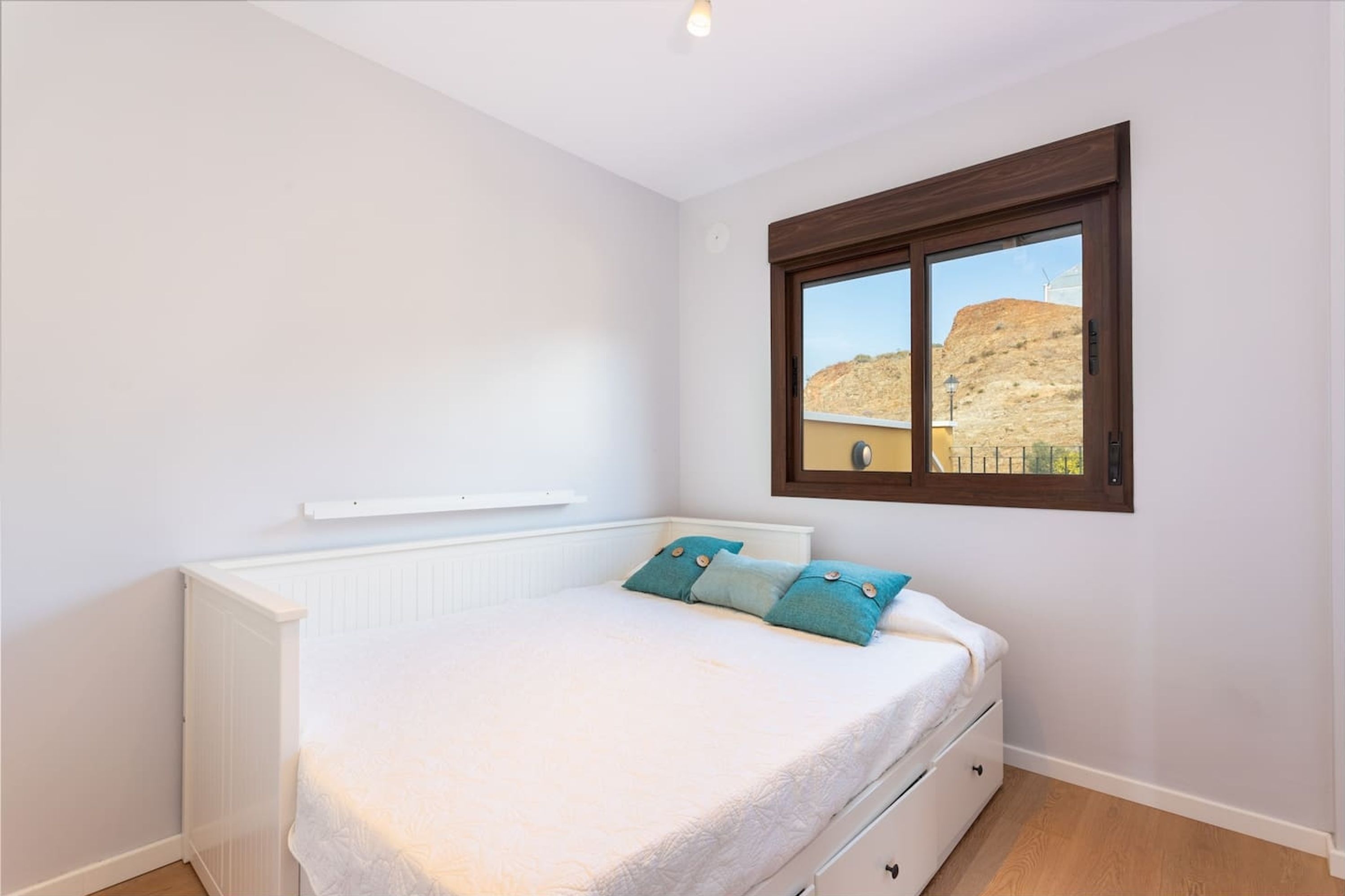 Een slaapkamer met een bed, een raam en een witte muur.