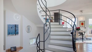 Una escalera moderna de diseño curvo, paredes blancas y un comedor con mesa y sillas.