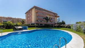 A swimming pool with a metal ladder, surrounded by a concrete deck. In the background, there is a multi-story building with balconies and a well-maintained lawn. - Duplex Algarrobo Costa Solset (Algarrobo)