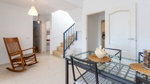 A modern living room with a glass dining table, a wooden rocking chair, a staircase, and a white door. - Duplex Algarrobo Costa Solset (Algarrobo)