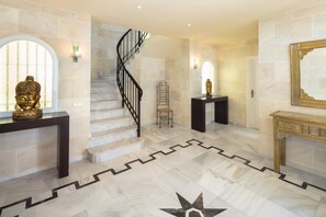 Un magnifique escalier avec une rampe noire menant à un palier, lequel est entouré d’un sol en marbre orné de motifs géométriques.