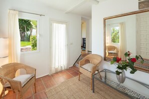 Une pièce comprenant deux fauteuils en osier, une table en verre, un miroir et un vase de fleurs.