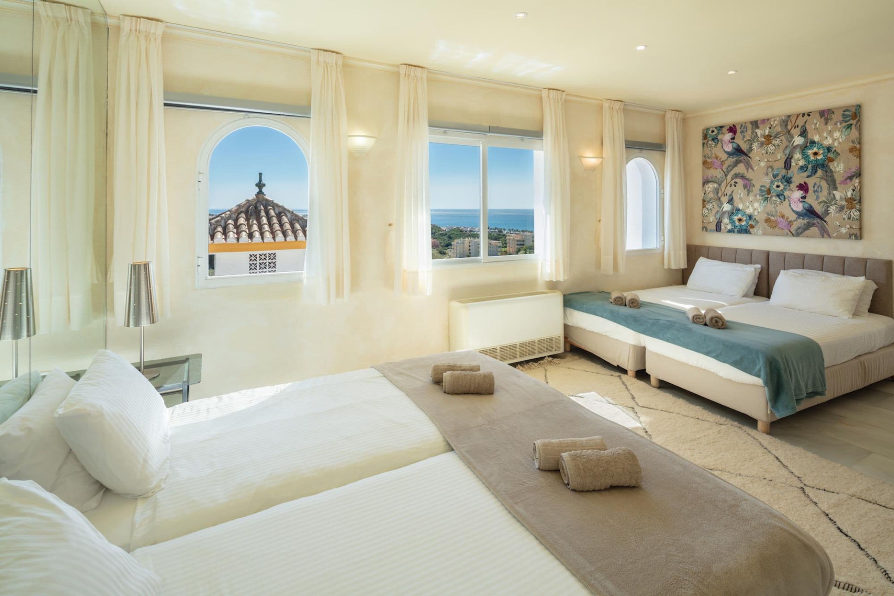 A hotel room with a large bed, a smaller bed, a view of the sea, and a painting on the wall.