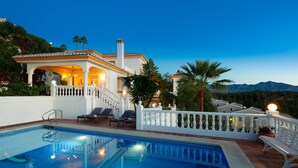 A poolside area with a clear view of a pool, a white building with a balcony, and a mountainous backdrop. - Large Luxury Family Villa 500m From Beach (Mijas)