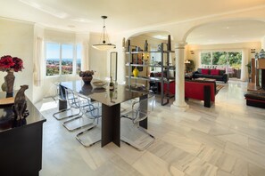 A spacious living area with a large island table, clear glass chairs, and a view of the outdoors. - Large Luxury Family Villa 500m From Beach (Mijas)