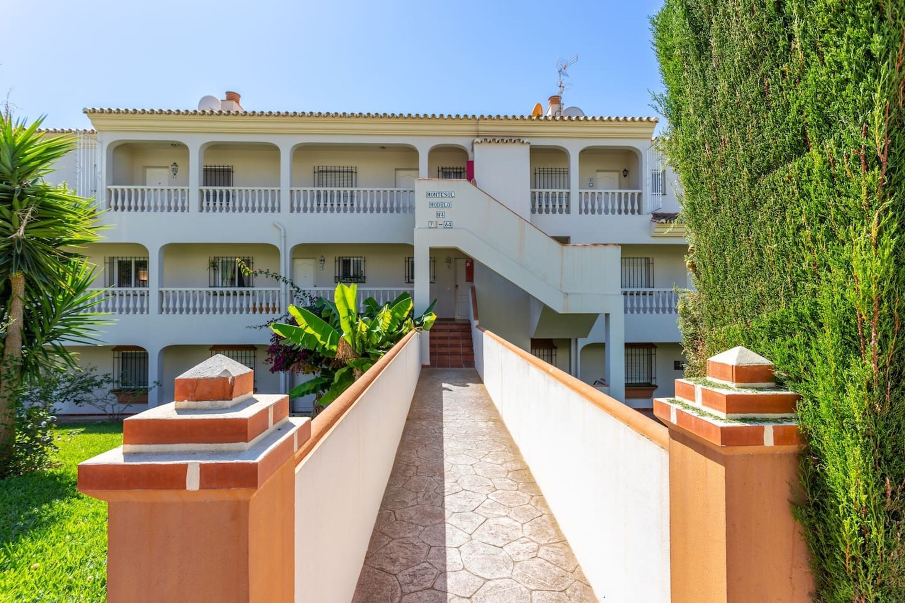 Um hotel com vários andares, uma escadaria central, varandas e um jardim bem cuidado.