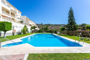 Una piscina con agua cristalina y azul, rodeada por un césped cuidado y un edificio con balcones.