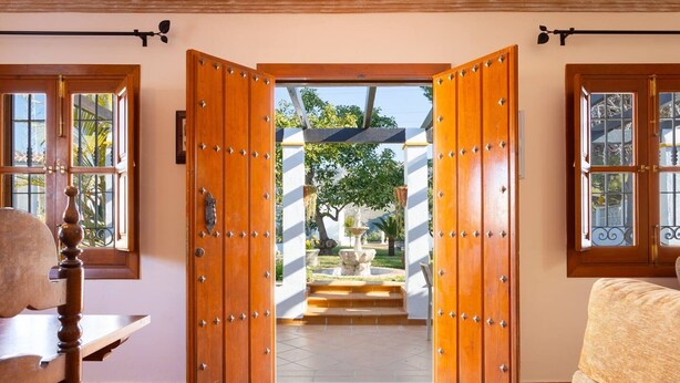 Une pièce dotée d’une grande porte en bois qui donne sur un espace extérieur avec des marches et une fontaine.
