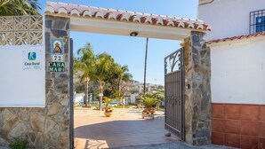 Une entrée fermée par un portail mène à une propriété appelée Casa Mari, qui se distingue par un arc en pierre et un toit recouvert de tuiles.
