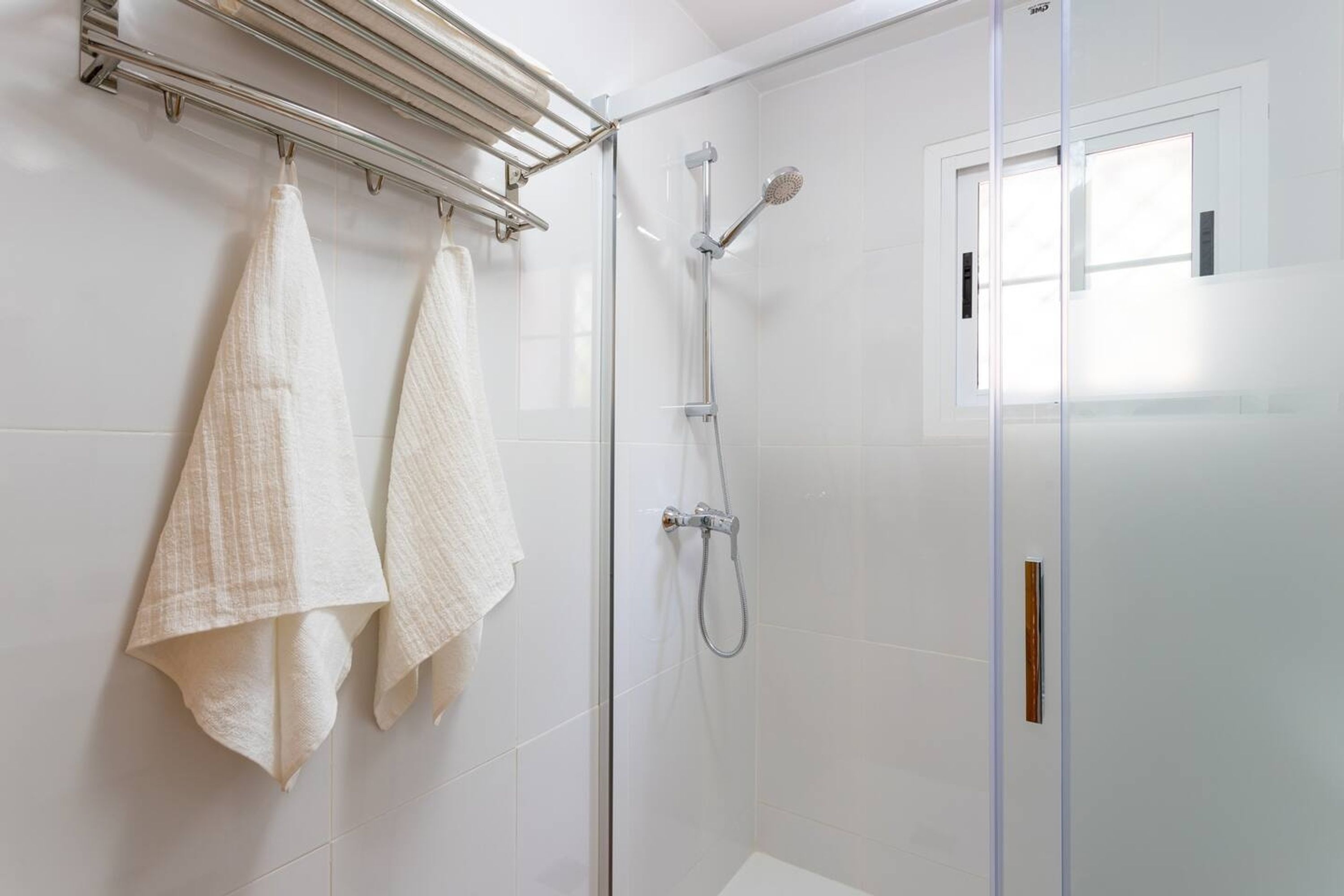A modern bathroom with a glass shower enclosure, a towel rack with two towels, and a window providing natural light.