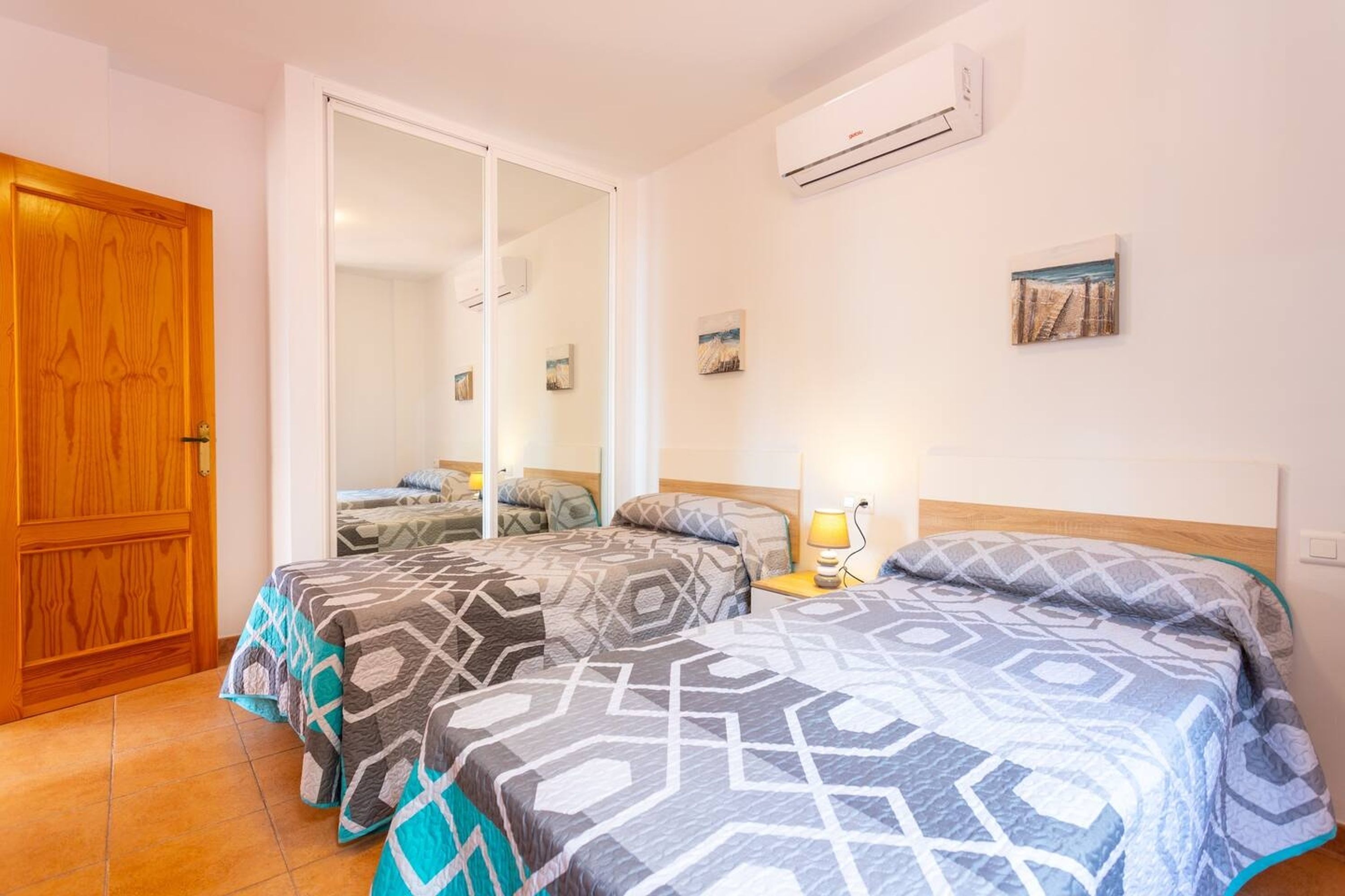 A bedroom with two beds, a wooden door, and an air conditioning unit on the wall.
