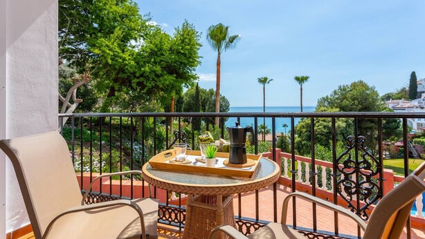 A balcony with a round table, two chairs, and a view of the sea. - Apartamento Ladera Solset (Nerja)