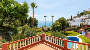 A balcony with a view of a pool, lush greenery, and a coastal landscape. - Apartamento Ladera Solset (Nerja)