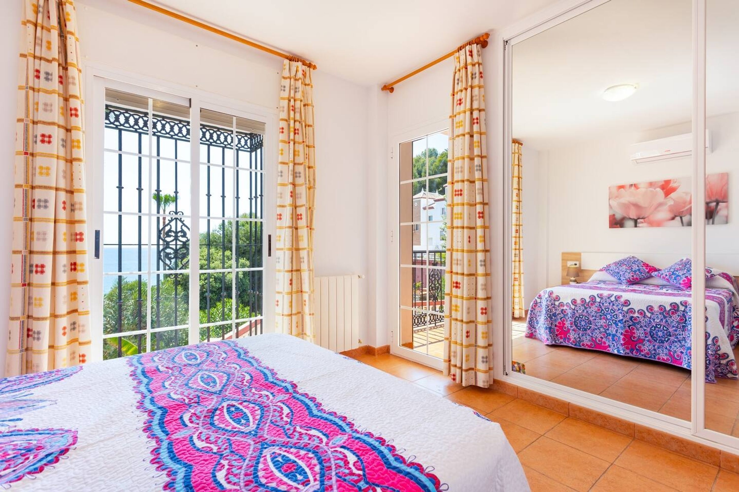 A bedroom with a large bed, a balcony with a view, and a sliding glass door leading to an outdoor area.
