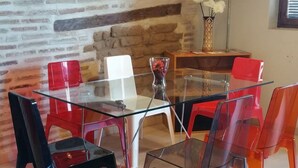 Uma área de refeições com mesa de vidro e cadeiras, parede de tijolos e luminárias pendentes.