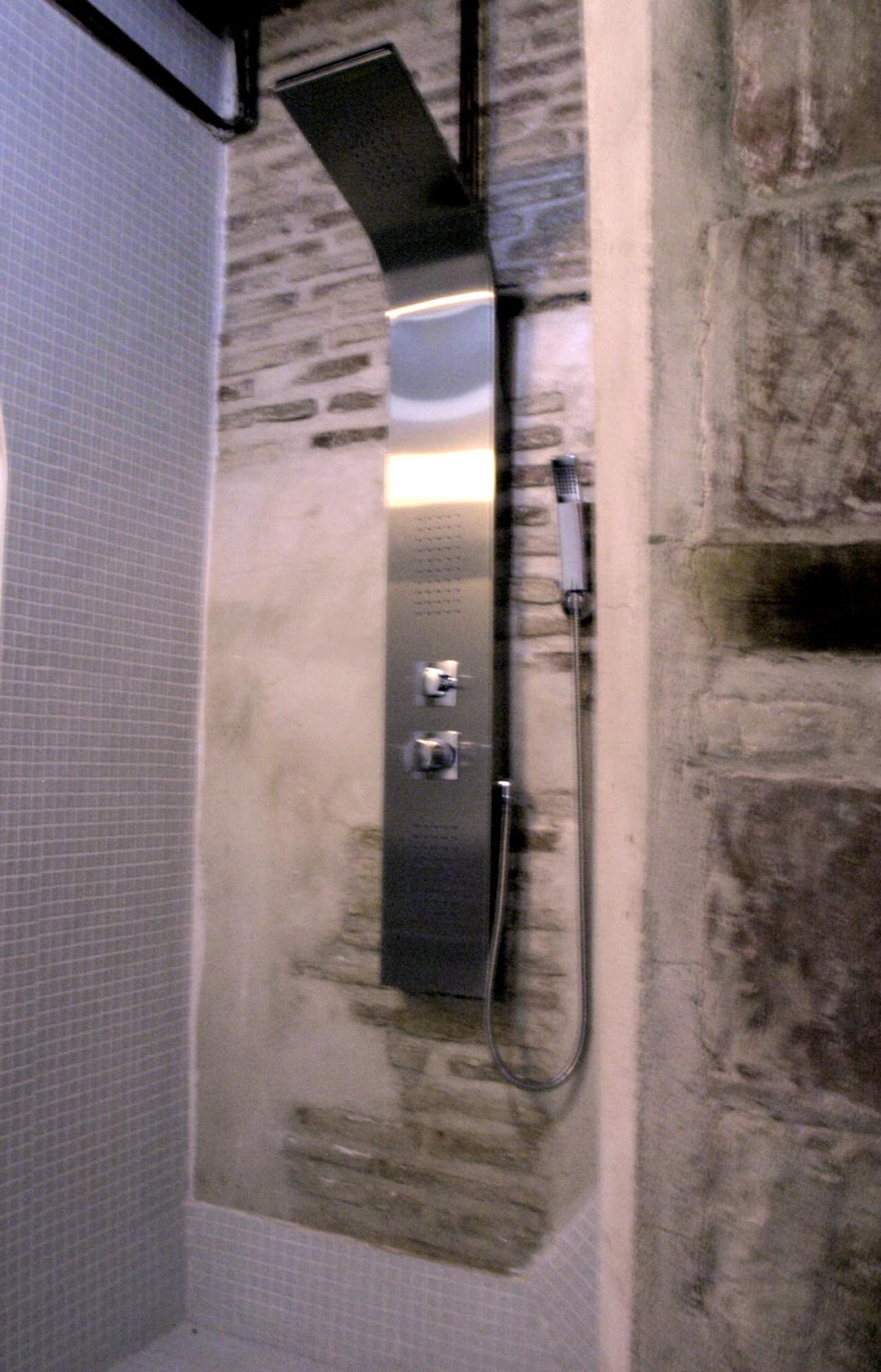 Un baño con pared de azulejos, pared de piedra y zona de ducha con panel de control.