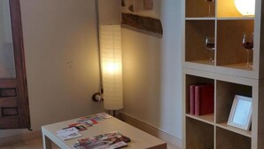 Quarto com parede de pedra, uma luminária grande, televisão de tela plana e uma estante com revistas.