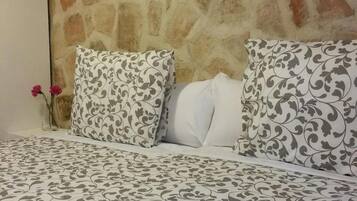 Una habitación con pared de piedra, una obra de arte enmarcada, una cama con ropa de cama estampada y un florero con una sola flor.