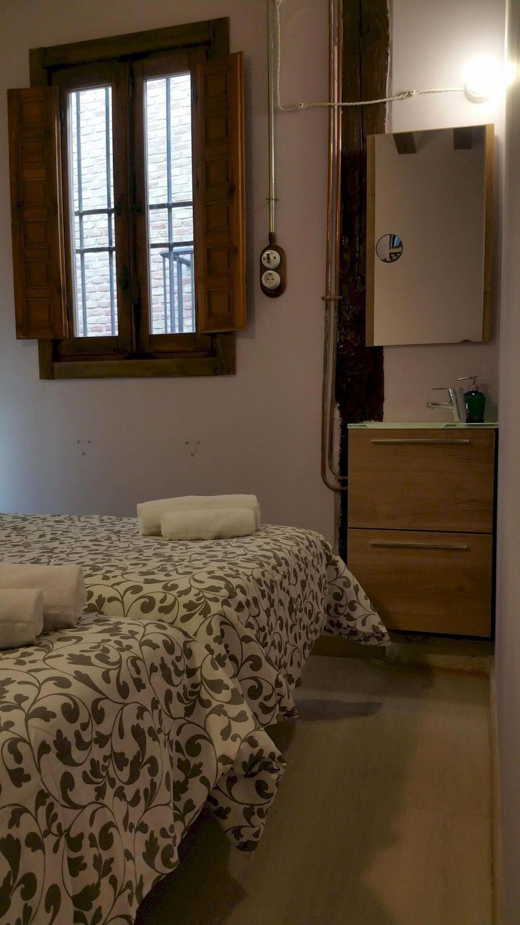 Een slaapkamer met een bed, een raam, een spiegel en een houten kast.