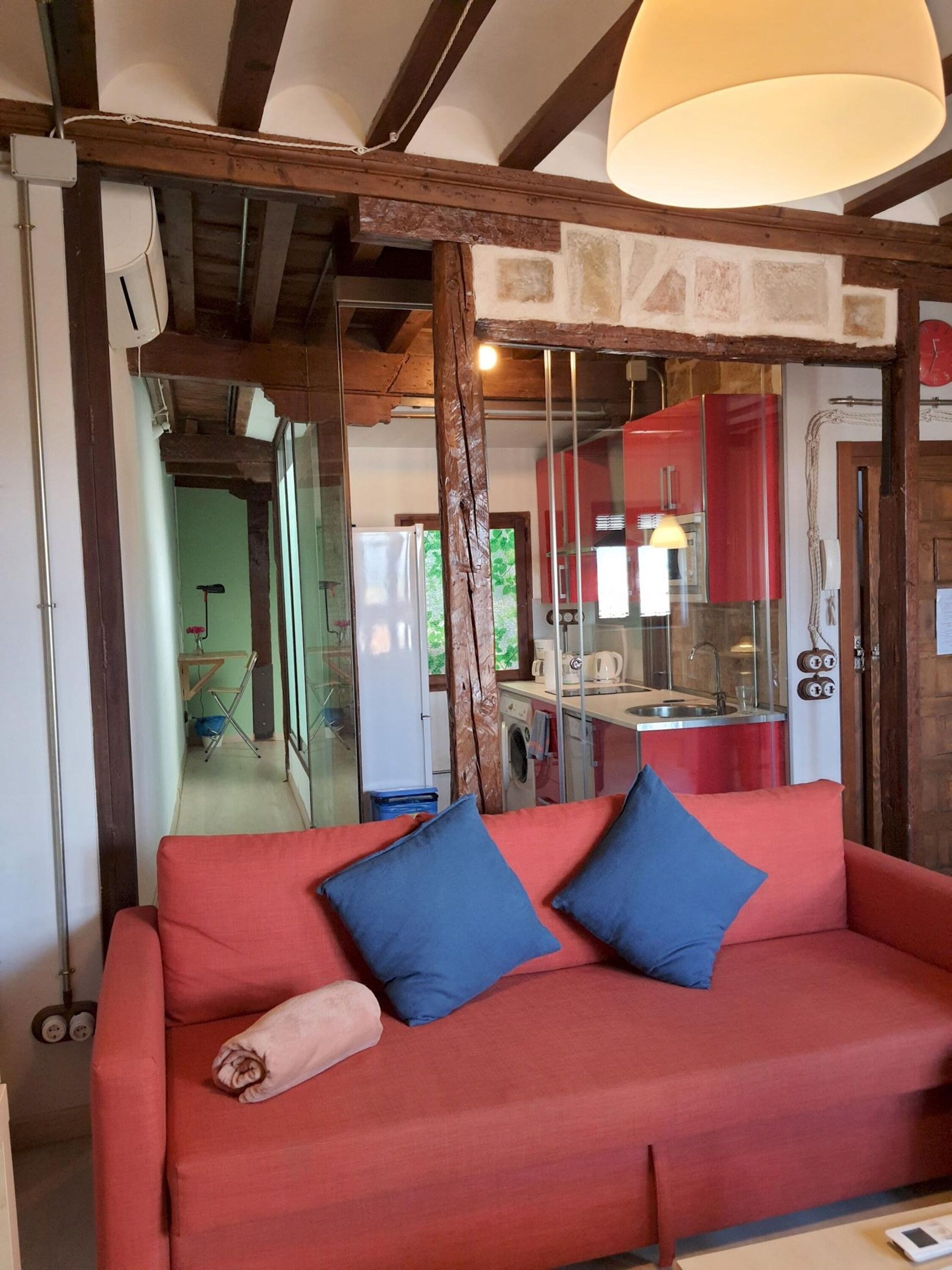 A modern interior with a red sofa, blue cushions, a wooden staircase, and a glass partition.