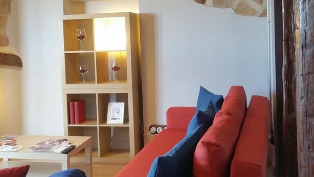 Uma sala de estar aconchegante com parede de pedra, teto de madeira e sofá vermelho com almofadas azuis.