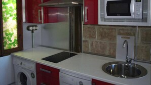 Uma cozinha compacta com armários vermelhos, uma pia de aço inoxidável, micro-ondas, forno embutido e máquina de lavar roupa.
