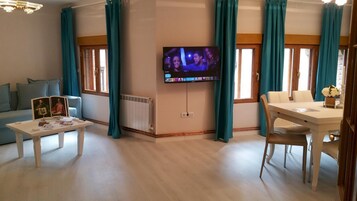 Una sala de estar con televisor, sofá, mesa de comedor y cortinas color turquesa.