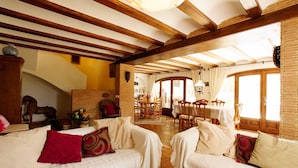 A spacious living area with high ceilings and exposed wooden beams, featuring two white sofas with red cushions, a dining area with wooden furniture, and large windows allowing natural light. - Villa La Siesta in Javea (Javea)