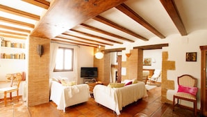 A spacious living room with exposed wooden beams, a brick wall, and a tiled floor. There are two white sofas, a television, and a bookshelf. - Villa La Siesta in Javea (Javea)