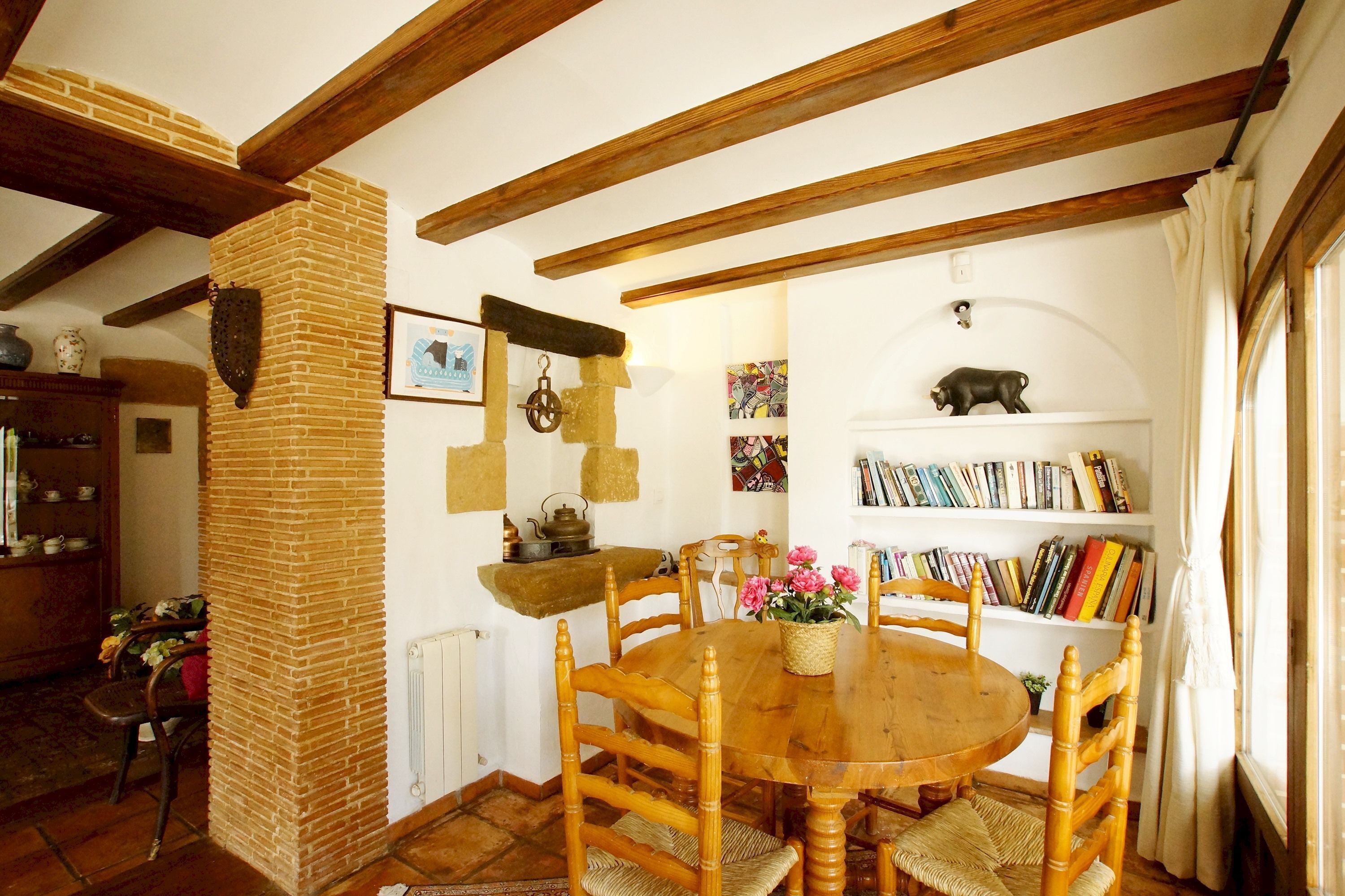 Ein gemütlicher Essbereich mit einem Holztisch und -stühlen, einem Kamin aus Ziegelsteinen und einem Bücherregal voller Bücher.