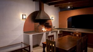 Una cocina al aire libre con horno de ladrillo, sillas de madera y una mesa de comedor.