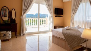 Habitación de hotel con cama, televisión, balcón con vistas a las montañas y ventana con cortinas.