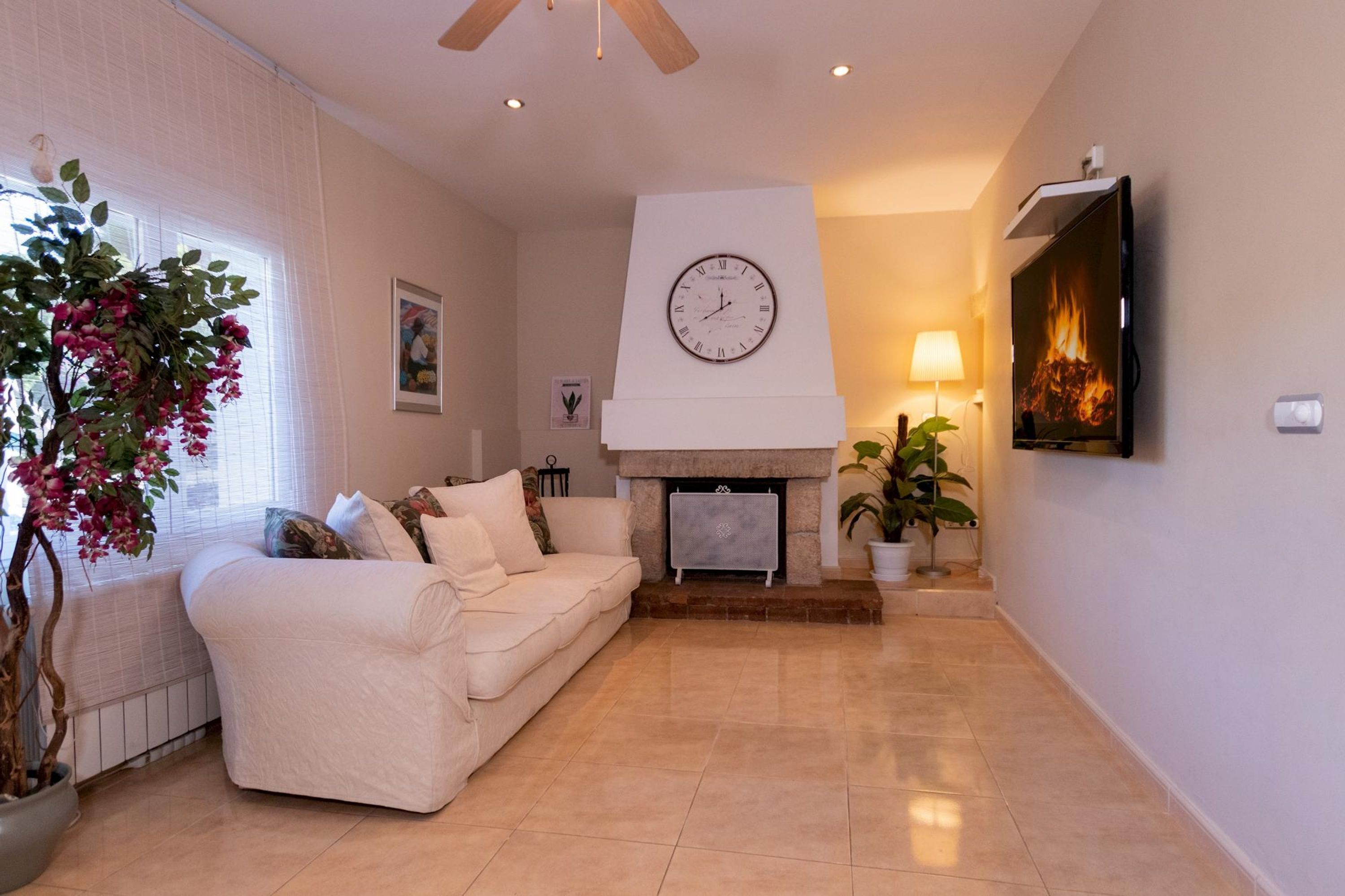 A living room with a white sofa, a fireplace, a clock, and a TV.