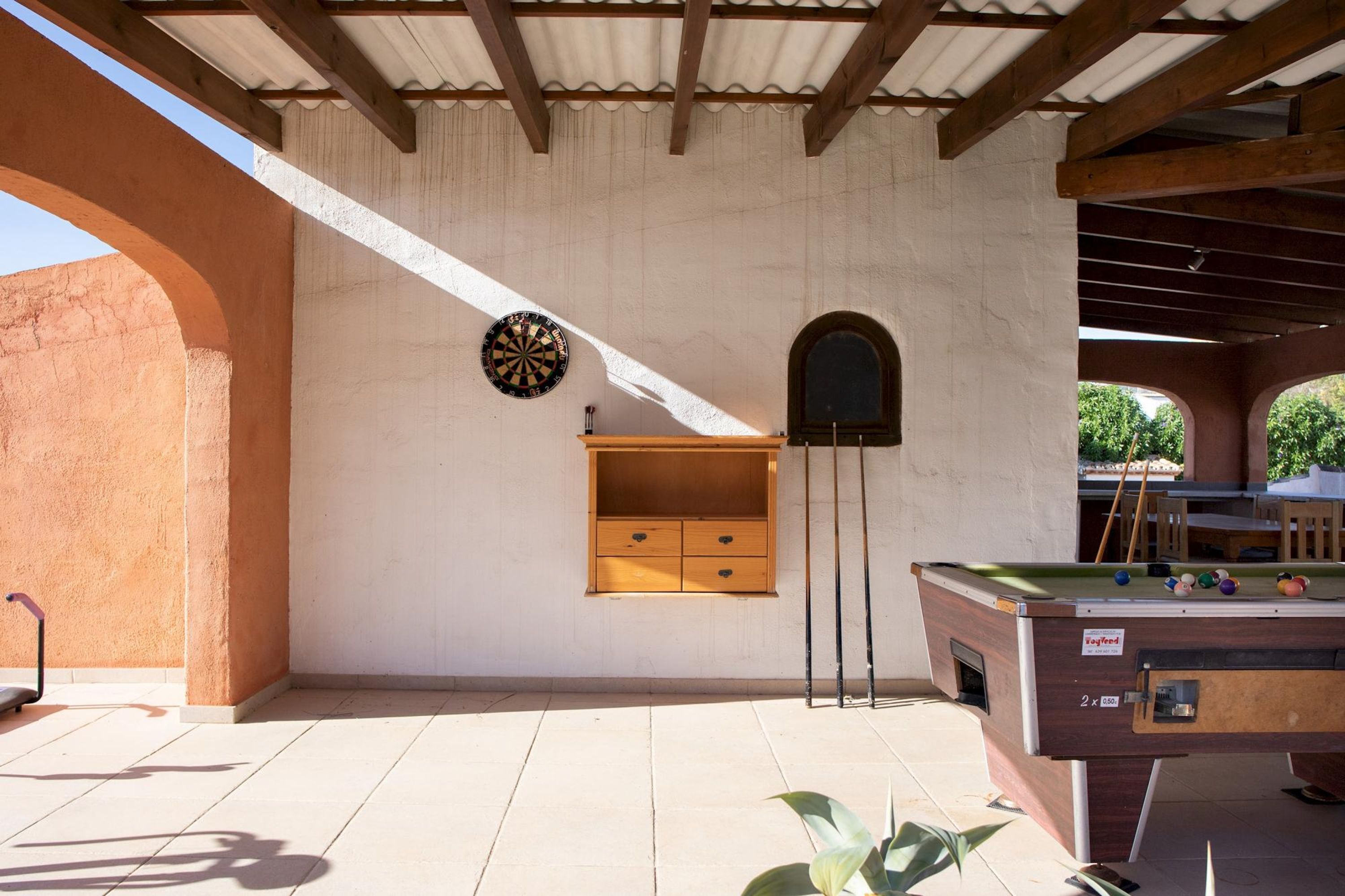 A billiards table with a dartboard and a small wooden cabinet against a wall.