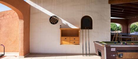 A billiards table with a dartboard and a small wooden cabinet against a wall.