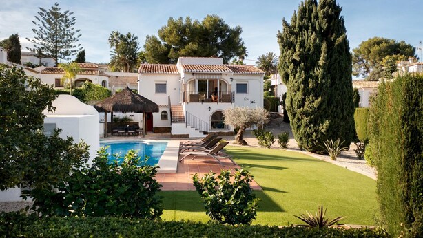 Een villa met een zwembad, een overdekt terras en een verzorgd gazon.