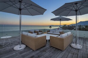 A deck with wicker furniture and umbrellas, overlooking a body of water and distant mountains. - Villa Frontline Beach Costabella - Marbella (Marbella)
