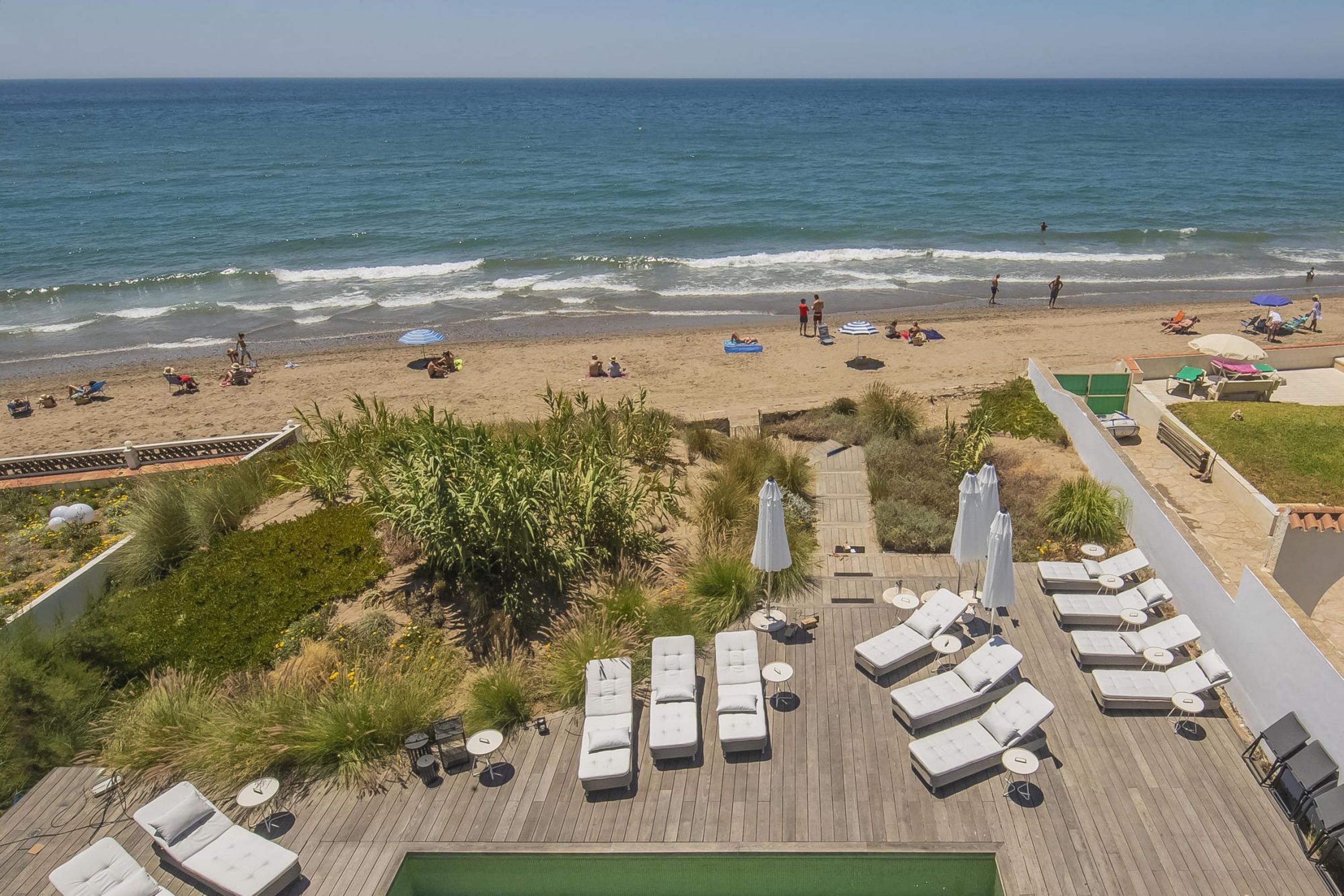 A beachside resort with sun loungers, a pool, and a view of the ocean.