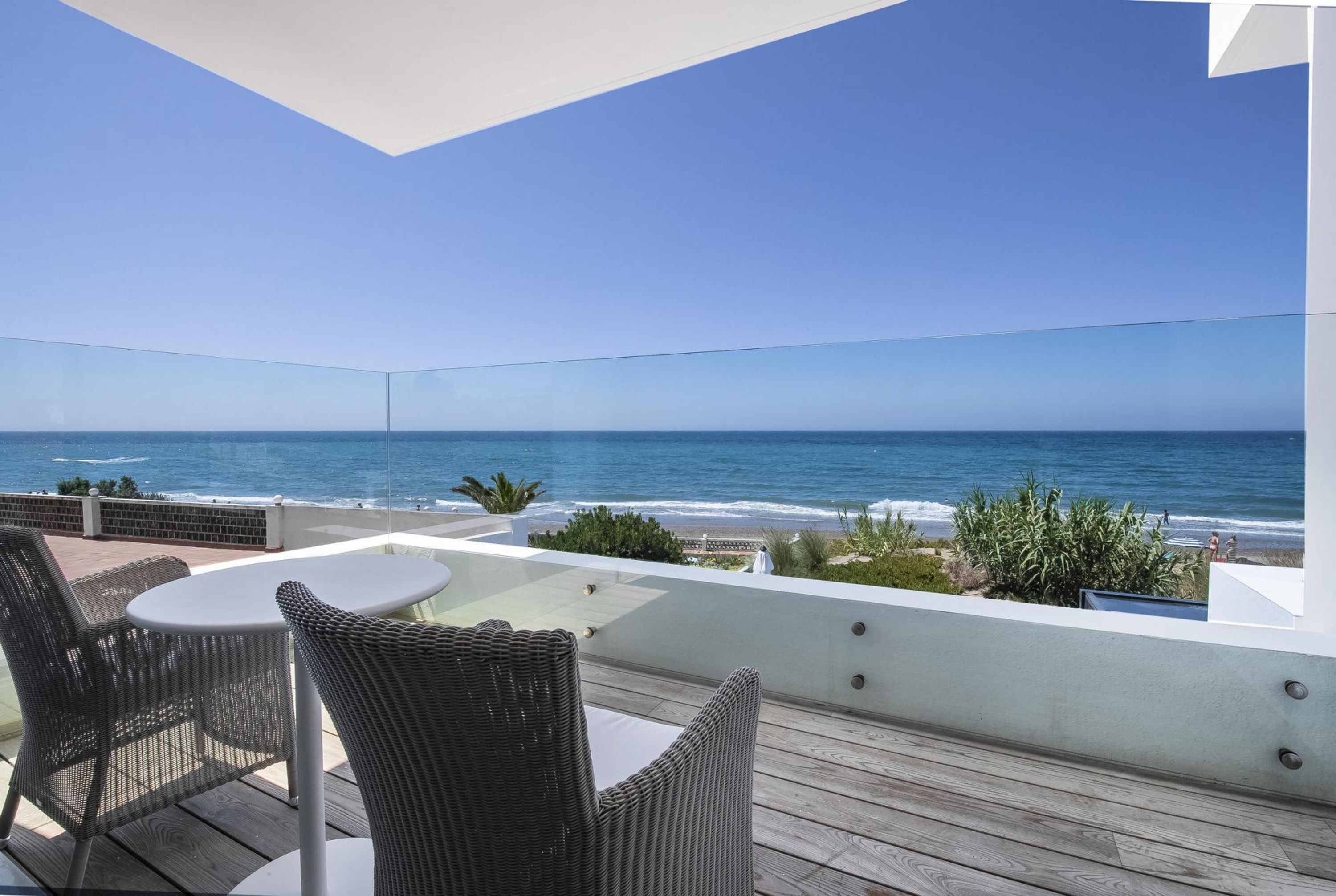 A balcony with wicker furniture and a glass table overlooking the ocean.