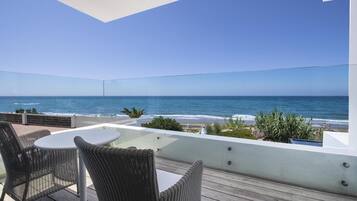 A balcony with wicker furniture and a glass table overlooking the ocean.