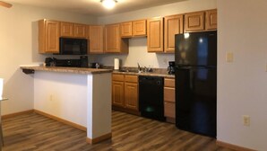 A kitchen with wooden cabinets, a black refrigerator, a dishwasher, and a microwave. - 2 Bedroom Apartment Next To Rivian (Bloomington)