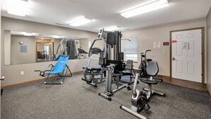 A gym with exercise equipment, a mirror, and a door. - 2 Bedroom Apartment Next To Rivian (Bloomington)