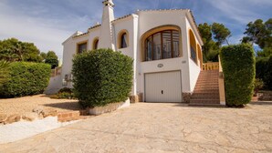 A white building with a tiled roof, a large arched window, and a staircase leading to a door.