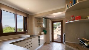 A modern kitchen with a large window, a sink, and a countertop. There are cabinets and a door leading to a balcony.