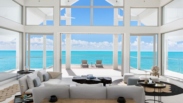 A spacious living area with a large window overlooking the ocean, furnished with a sofa, coffee table, and chairs.